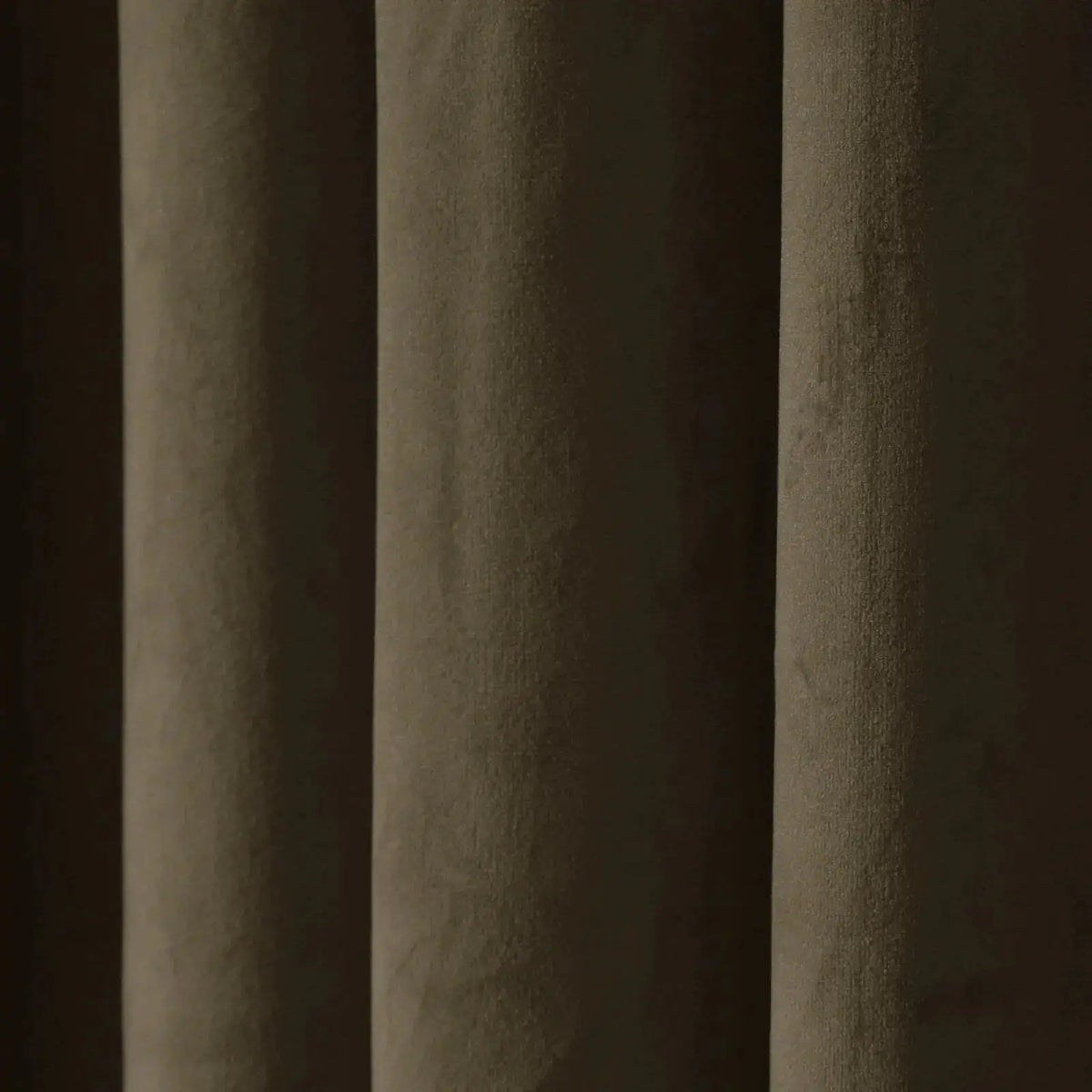A close-up of a dark brown textured curtain featuring deep vertical folds, a velvety fabric surface, and muted olive-green and dark brown tones highlighted by soft light